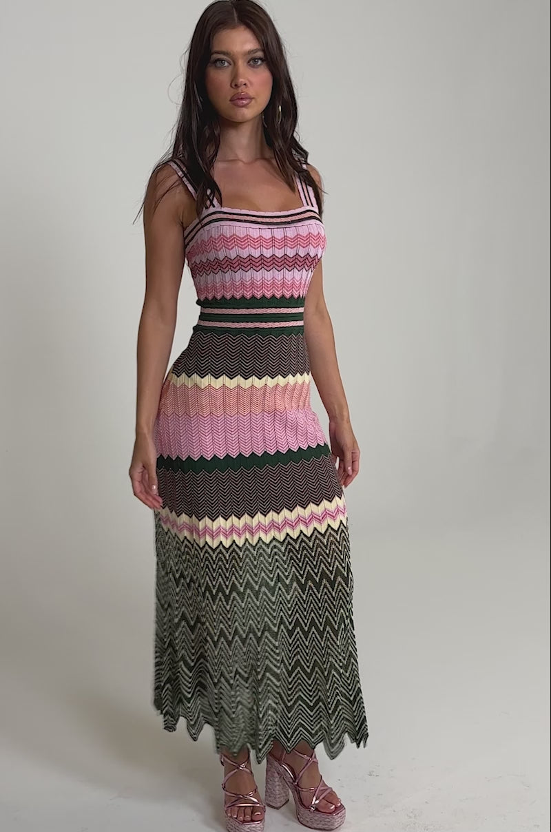 Video of woman modeling the HEAT WAVE KNIT MAXI DRESS, a sleeveless pink chevron maxi with black, yellow, and green zigzag patterns, styled with pink platform shoes against a plain light background.