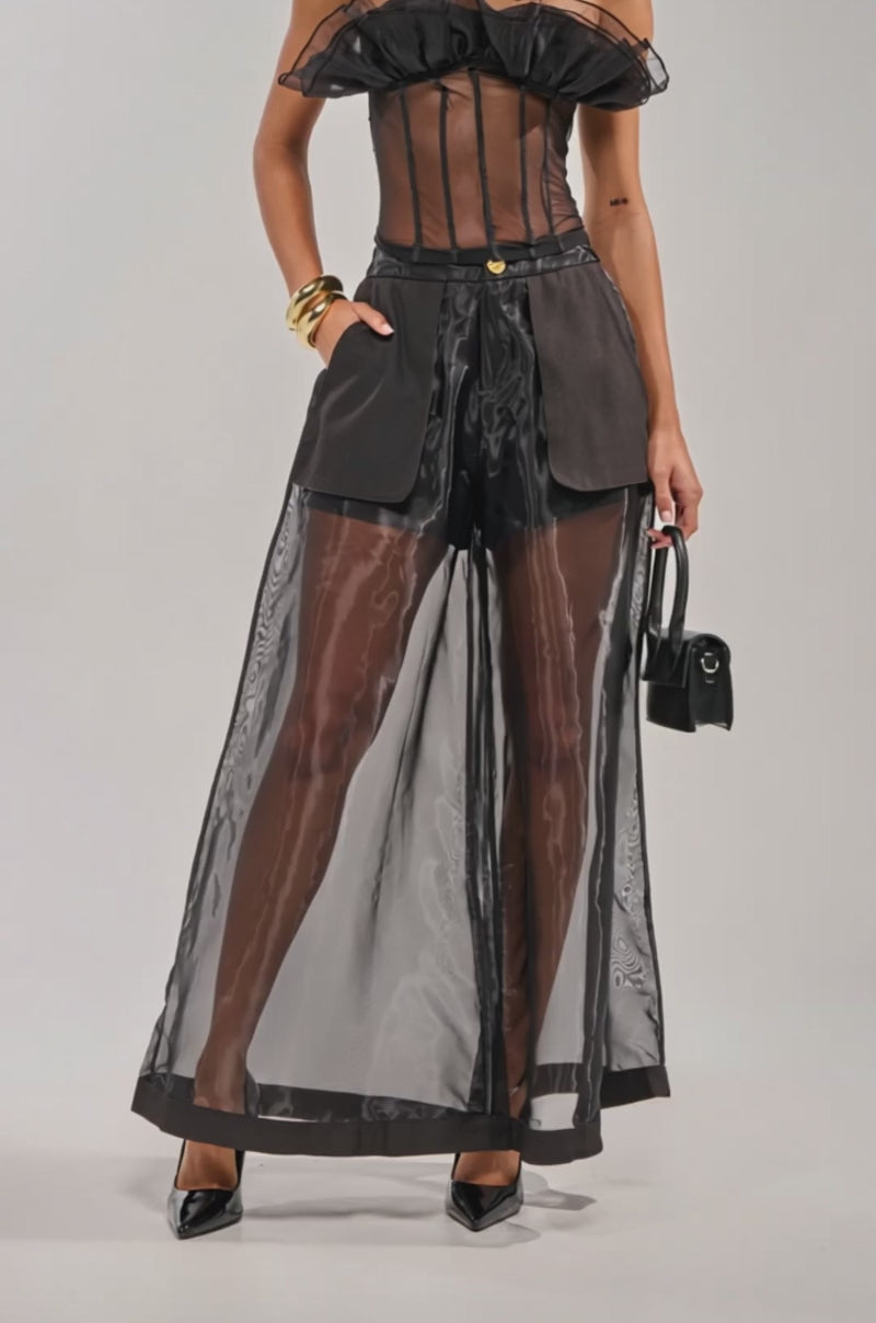 Video of woman modeling the FANCY LIKE ME TROUSER, mesh wide-leg pants. She accessorizes with hoop earrings, gold bangles, a small black handbag, and black heels.