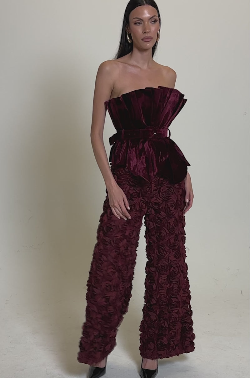 A video of a woman wearing the DRAMA DRAMA DRAMA VELVET BLOUSE, a strapless peplum-hem top, styled with wide-leg rose-patterned pants, a matching belt, and black pointed-toe heels.