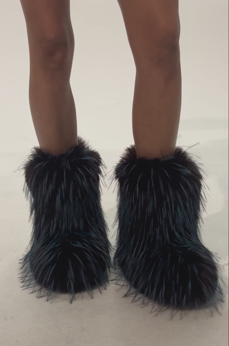 Video of woman modeling the AZALEA WANG LENIX BLUE MULTI FLAT FUR BOOTIE, showing only the boots and lower legs in view against a light background. The booties feature fluffy faux fur with dark brown and blue streaks.