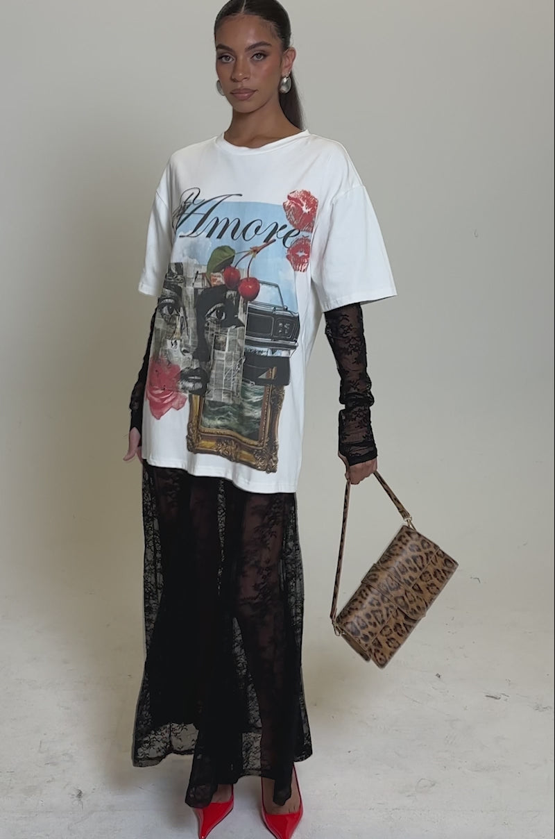 A video of a woman wearing the GIRLY BUT NOT LAYERED LACE MIDI DRESS WITH GRAPHIC. She's carrying a leopard print handbag, wearing red heels and hoop earrings, and standing against a plain light background with her hair pulled back.