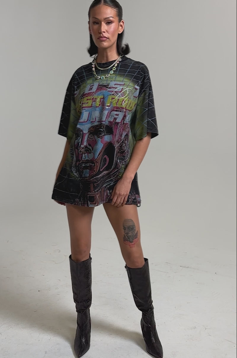 A video of a woman wearing the NEW METAVERSE OVERSIZED GRAPHIC TEE with a vibrant abstract face, paired with knee-high boots. 