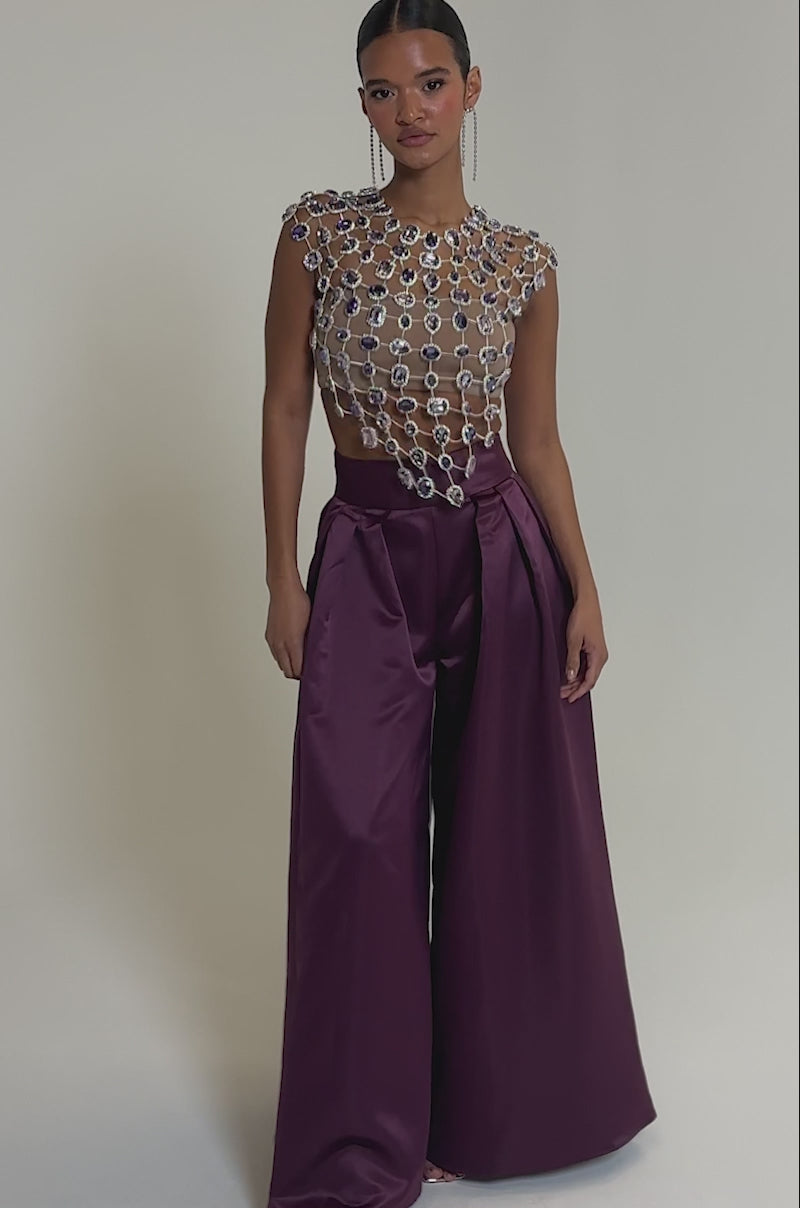 Video of woman modeling the LOVER GIRL RHINESTONE CHAIN TOP, featuring jeweled embellishments and a grid of large crystals. She pairs it with long, sparkling earrings and wears her hair slicked back.