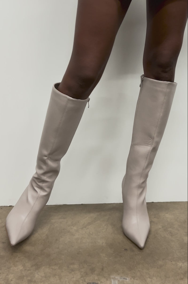 Video of woman modeling the AZALEA WANG GAMMA GREY CHUNKY KNEE HIGH BOOTS, standing against a white wall with one leg slightly bent; the background is a plain concrete floor.