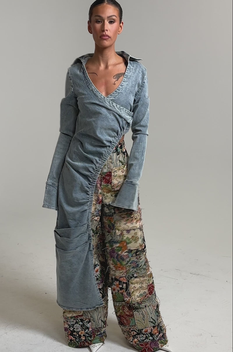 Video of woman modeling the GET MY CLOSE UP EMBELLISHED BUTTON DOWN SHIRT, paired with loose, high-waisted, floral patchwork pants and pointed white shoes against a simple studio backdrop.