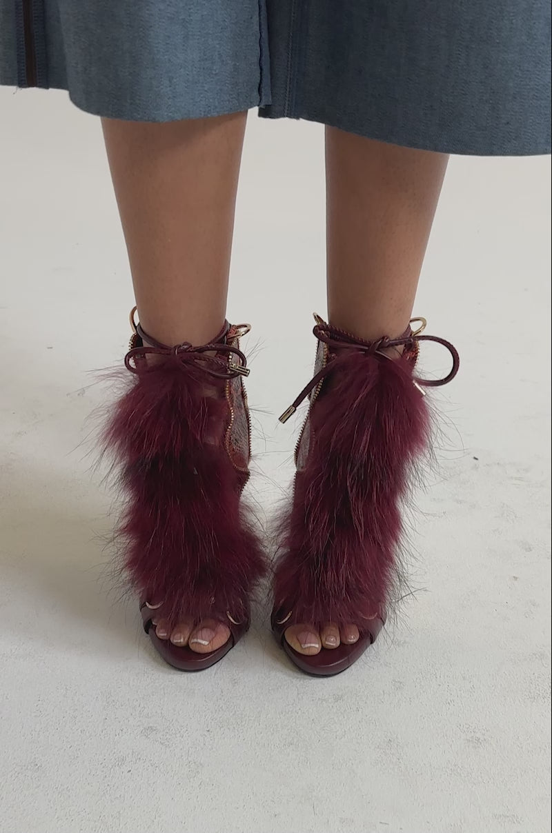 A video of a person wearing the AZALEA WANG SHAINY SNAKE BURGUNDY MULTI open-toe stiletto sandals with red faux fur, gold hardware, snake print leather, and a lace-up front.