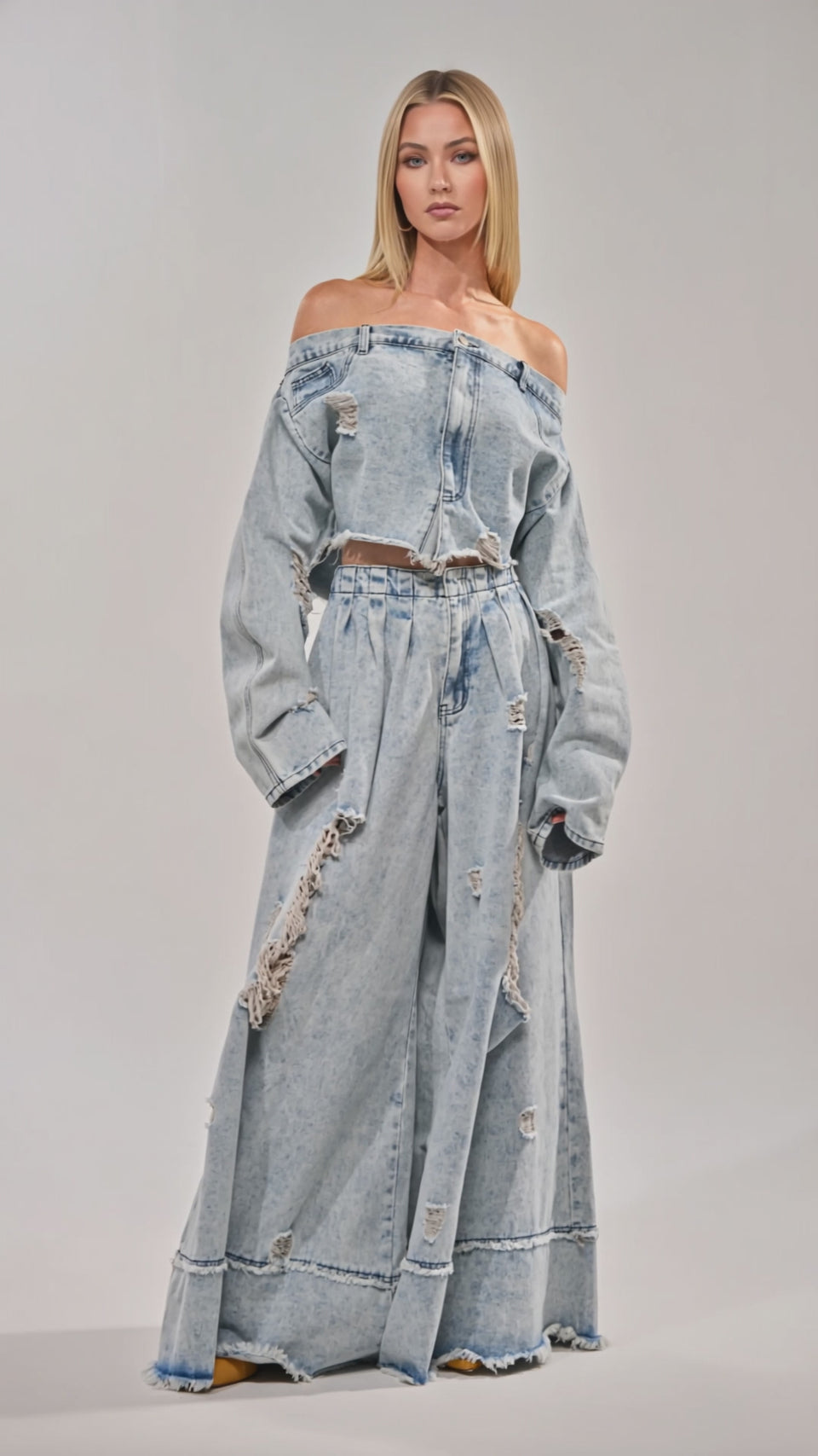 Video of woman modeling the CAMILLE DENIM BLOUSE, a loose-fitting, off-the-shoulder top, paired with ripped denim pants against a plain light background.