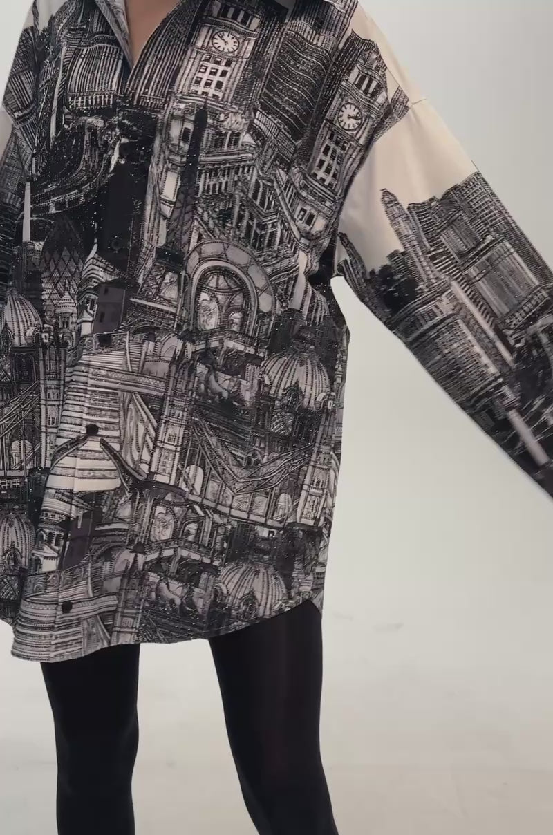 Video of a woman modeling the ALL AROUND THE WORLD POPLIN MINI DRESS, a graphic shirt dress adorned with detailed black and white architectural prints.