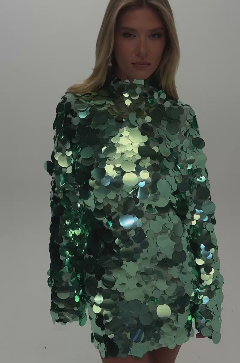 Video of a woman modeling the SPOILED & STUNNING LONG SLEEVE SEQUIN MINI DRESS in emerald green with a high neck and long, flared sleeves.