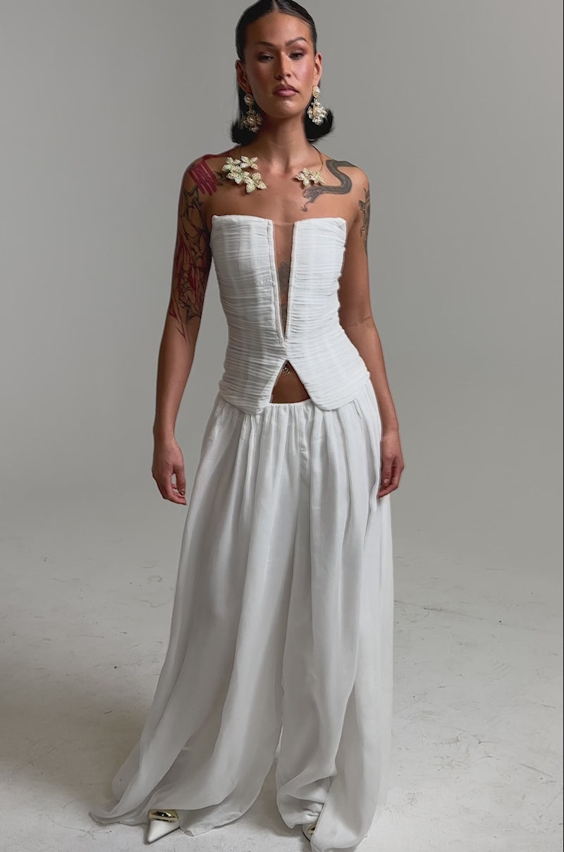 A video of a woman in the BEAUTIFUL WHITE PALAZZO PANT, featuring a strapless fitted bodice and sheer, wide-leg skirt.