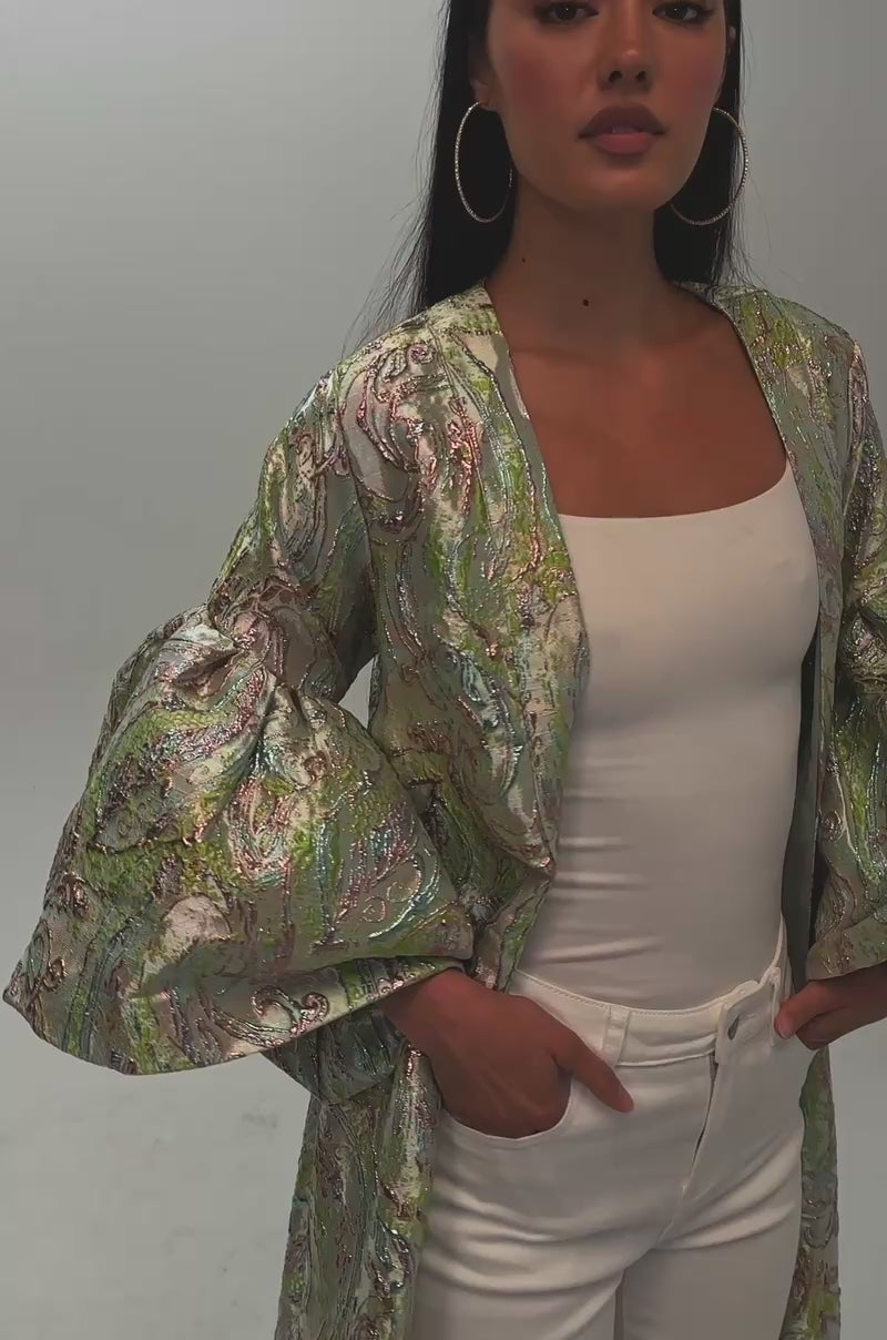 Video of a woman modeling the KEY LIME BROCADE DUSTER—a floor-length, light-colored brocade piece with voluminous paisley-patterned sleeves.