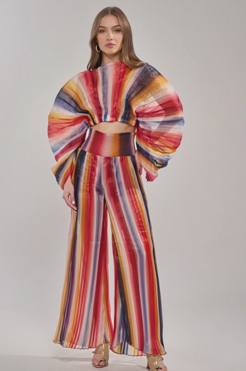 Video of woman modeling the FANNED OUT CHIFFON BLOUSE, a colorful sheer top with wide fan sleeves, paired with high-waisted pants featuring bold red, yellow, orange, blue, and white stripes.