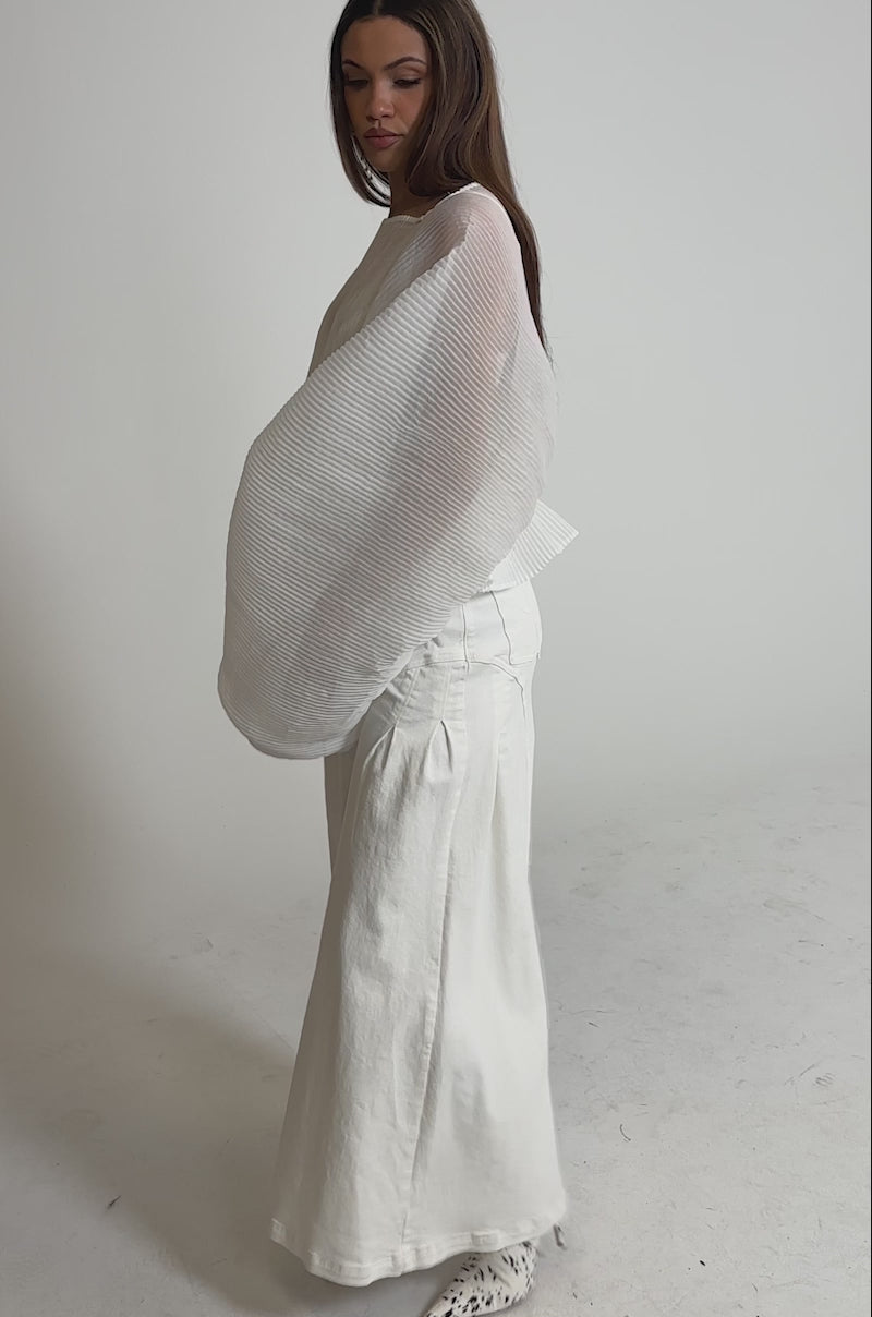 Video of woman modeling the PRETTY GIRL PROBLEMS BLOUSE IN WHITE—sheer, pleated chiffon with voluminous sleeves—pairing it with high-waisted white pants and posing confidently against a plain backdrop