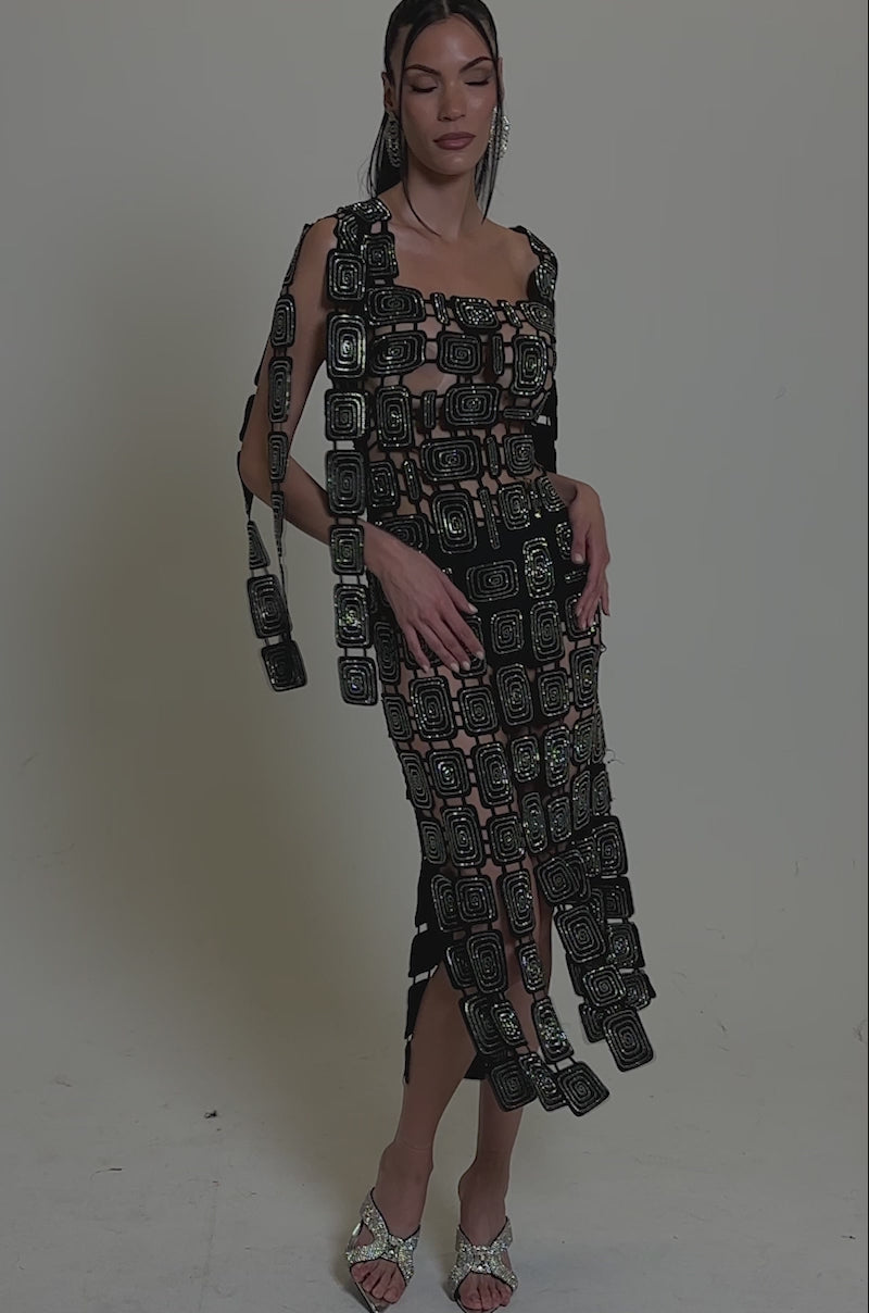Video of woman modeling the ONLY ONE OF ME RHINESTONE MIDI DRESS—a sheer black, bodycon midi with geometric rhinestone patterns—paired with long hair, large earrings, and open-toed heels in a neutral studio setting.