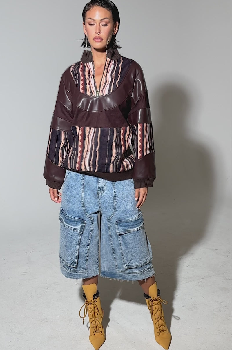 Video of woman modeling the CRAZY IN LOVE FAUX LEATHER SWEATSHIRT, featuring an abstract striped print in maroon, brown, and pink with faux leather details, paired with blue denim jeans against a plain light background.