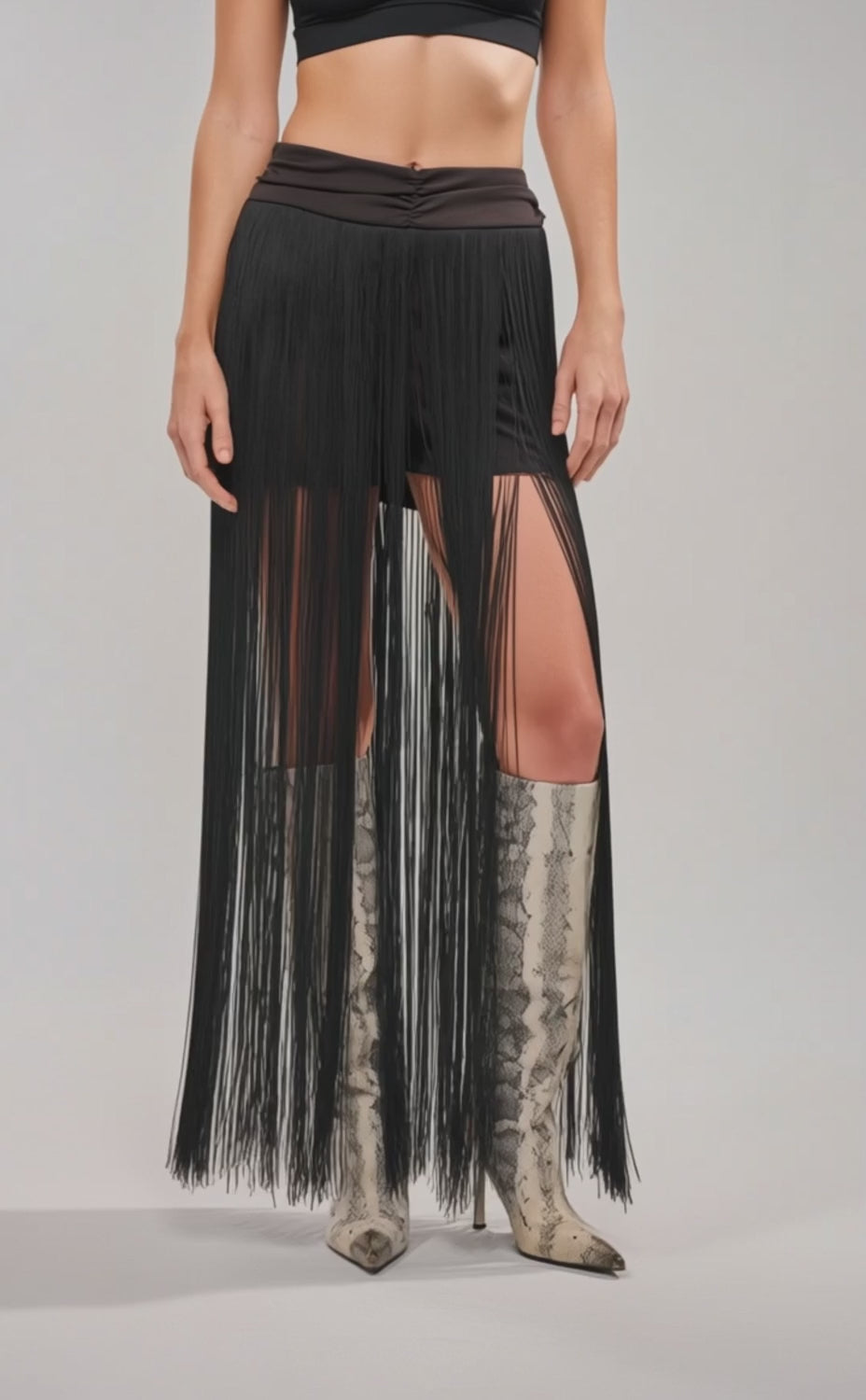 Video of woman modeling the ON THE EDGE FRINGE SKIRT IN BLACK, featuring a ruched waistband and long black fringe, paired with silver pointed-toe boots. 