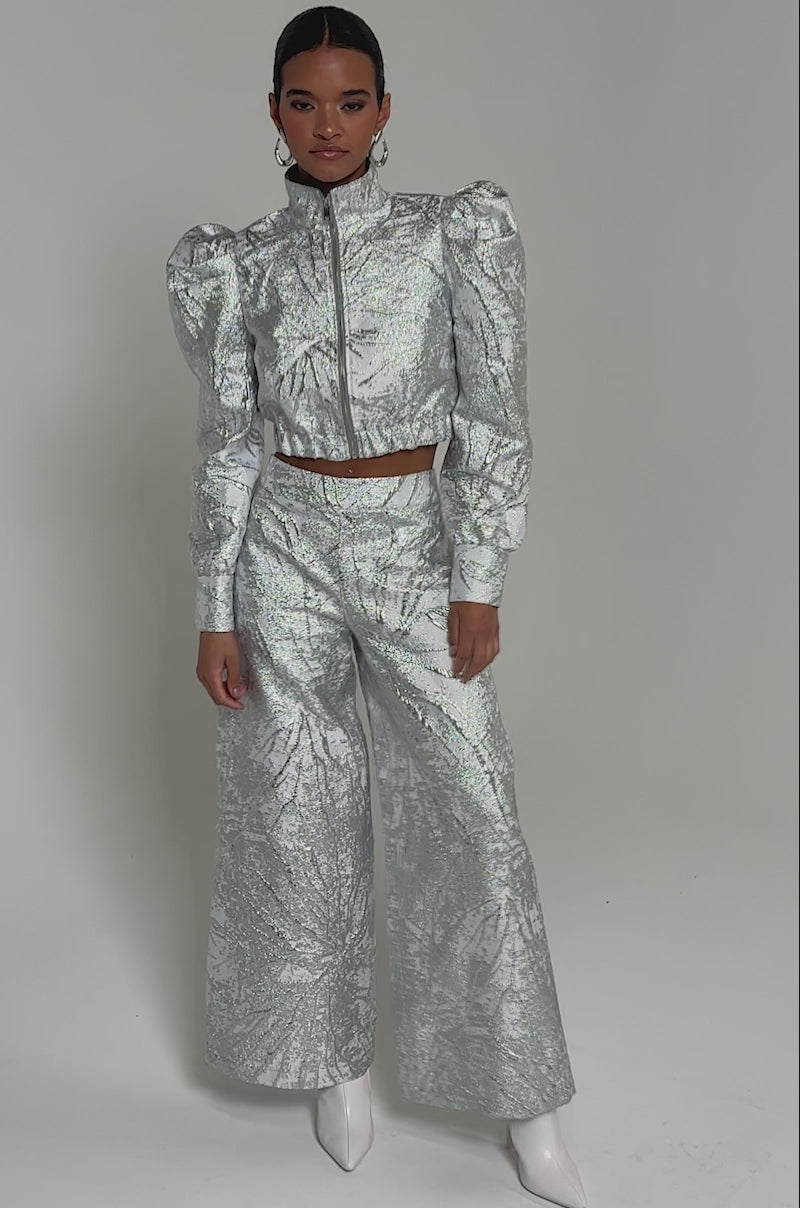 Video of woman modeling the JUST LIKE THAT BROCADE PANT—high-rise, wide-leg pants in silver metallic with a leaf-like pattern—paired with a matching cropped jacket and white pointed-toe shoes.