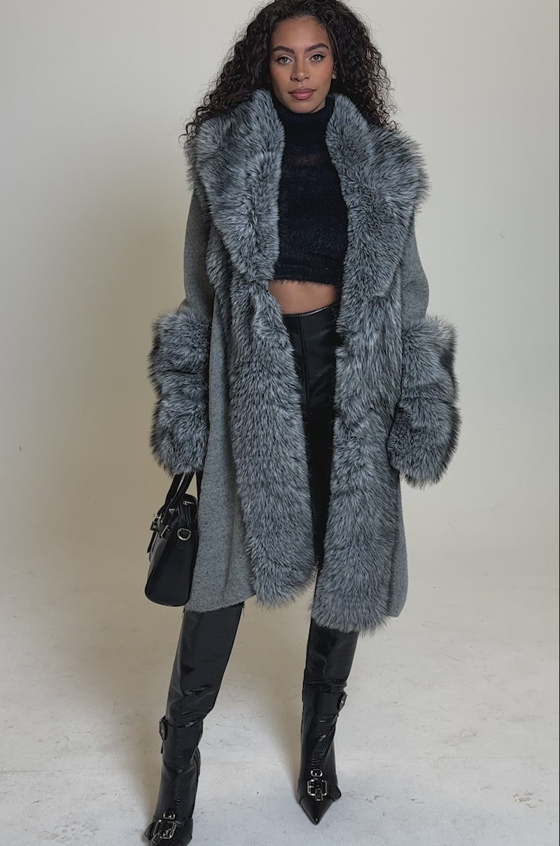 Video of woman modeling the RICH FLEX LONG CARDIGAN featuring thick, fluffy faux fur trim and cuffs over an oversized sweater. She holds a black handbag and stands confidently against a plain background.