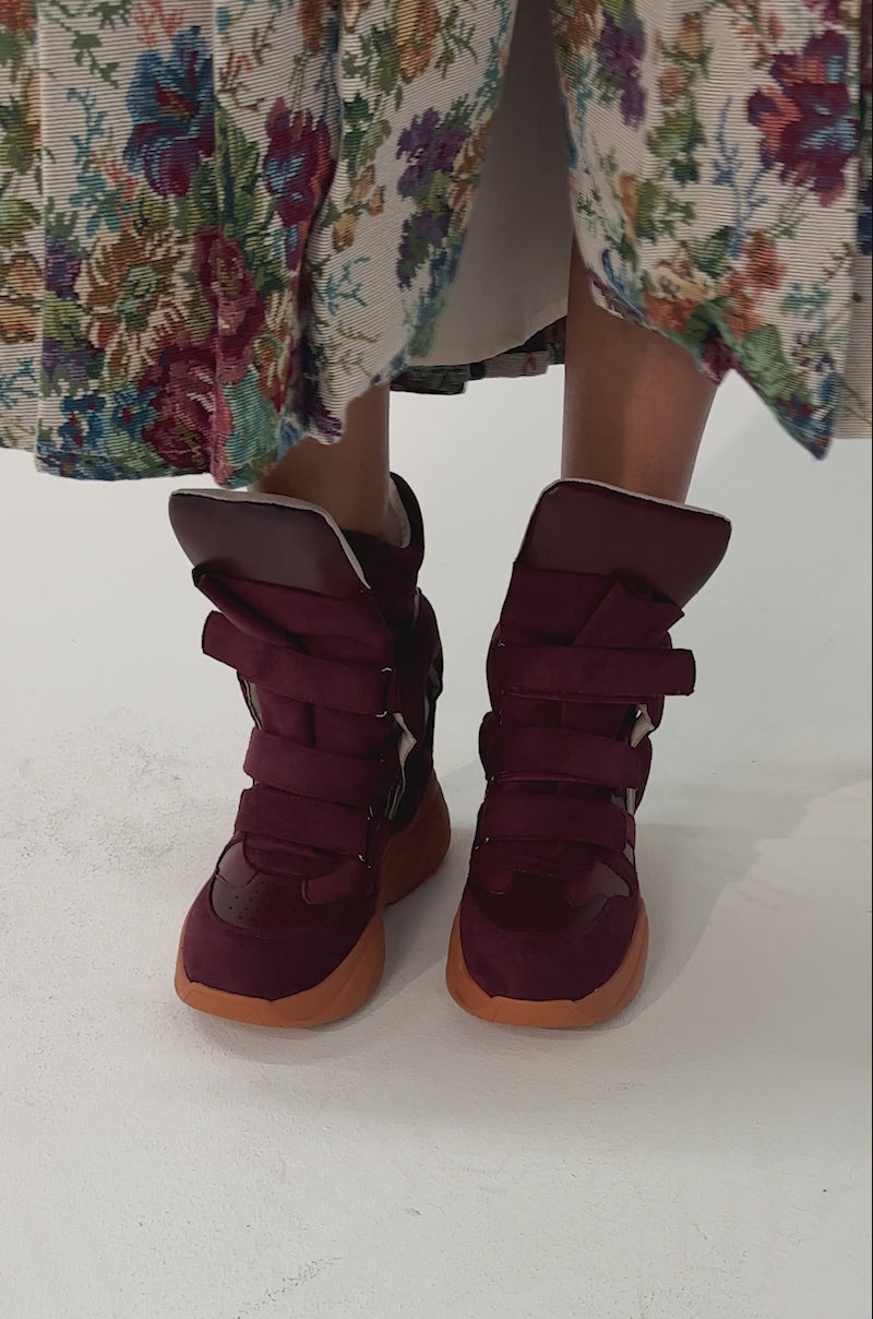 Video of woman modeling the MARANTO BURGUNDY WEDGE FAUX SUEDE SNEAKERS with thick soles and wide straps stands on a light-colored surface.