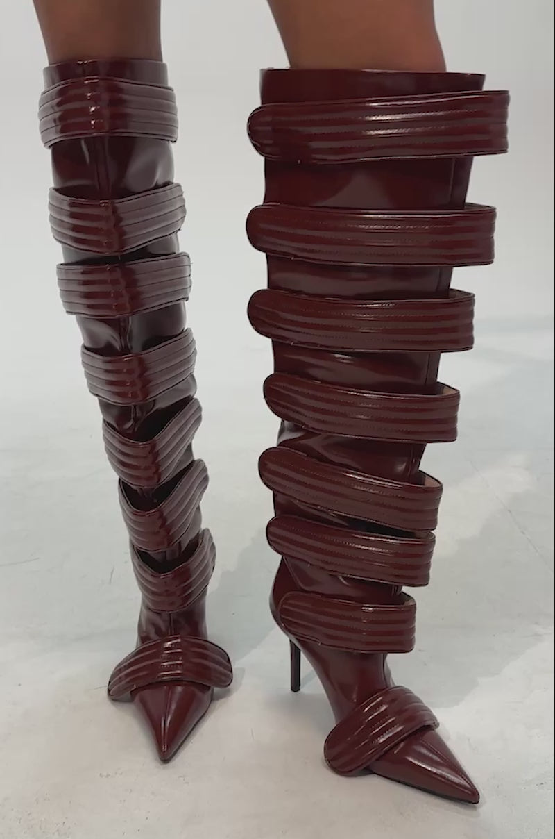 Video of woman modeling the AZALEA WANG JETSET COGNAC STILETO BOOT, featuring high, shiny brown leather with multiple thick horizontal straps and pointed toes