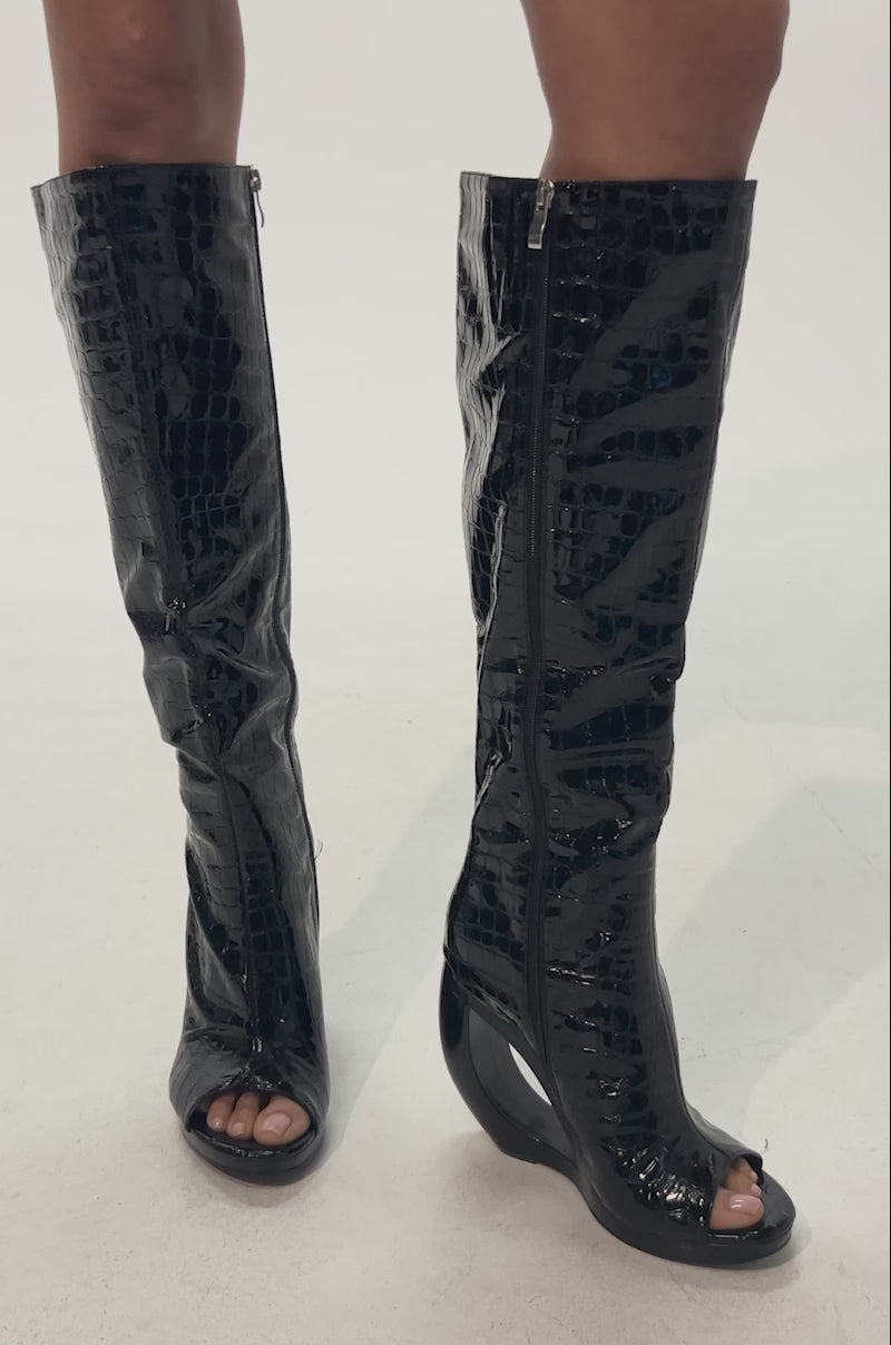 Video of woman modeling the AZALEA WANG CAMILLA BLACK CROC OPEN TOE WEDGE BOOT—knee-high, croc-embossed faux leather boots with curved wedge heels—against a plain light background.