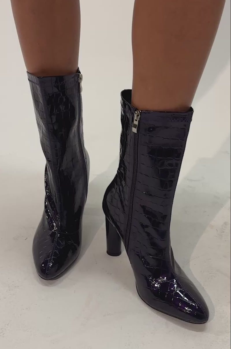 Video of a woman modeling the AZALEA WANG WINGROVE PURPLE CROC BLOCK BOOTIE—shiny, dark purple booties with a croc-embossed finish, a sleek silhouette, and chunky heels.