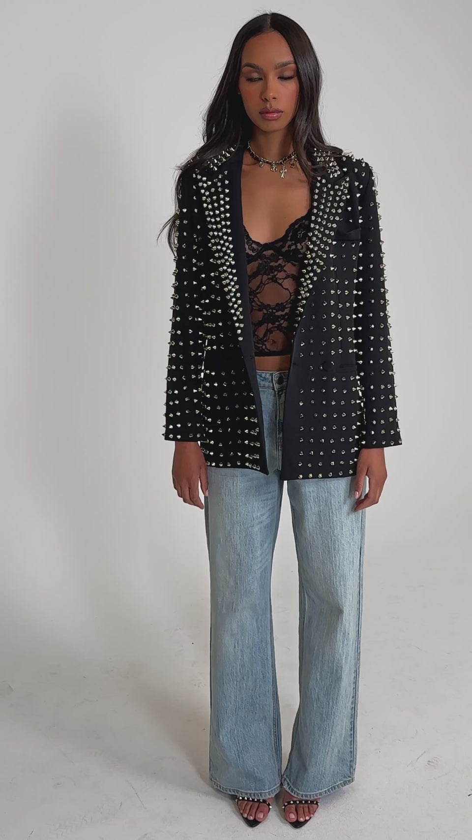 Video of woman modeling the SUGAR AND SPICE SPIKED STUD BLAZER over a black lace top, light blue wide-leg jeans, black strappy heels, and holding a small black handbag.