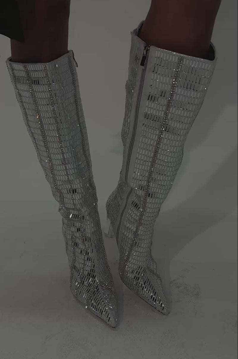 Video of a woman modeling the AKIRA GOLD GLOW UP SILVER CRYSTAL BLOCK BOOT—knee-high boots adorned with silver crystals, block heels, and rhinestone detailing.