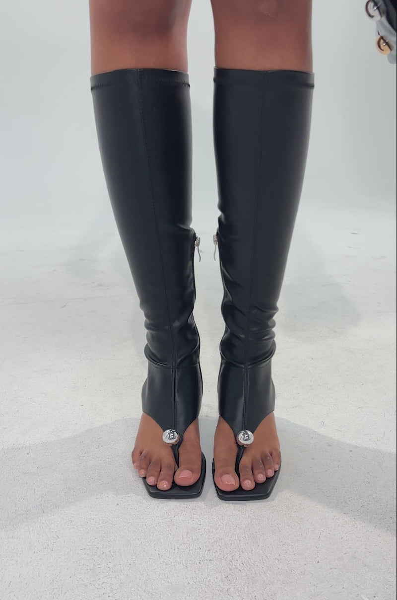 A video of a person wearing a black mini skirt with metallic studs, holding a matching studded handbag, and pairs the look with the AZALEA WANG DIPPIN DOT BLACK STRETCH SANDAL BOOT featuring sculptural heels against a neutral background.