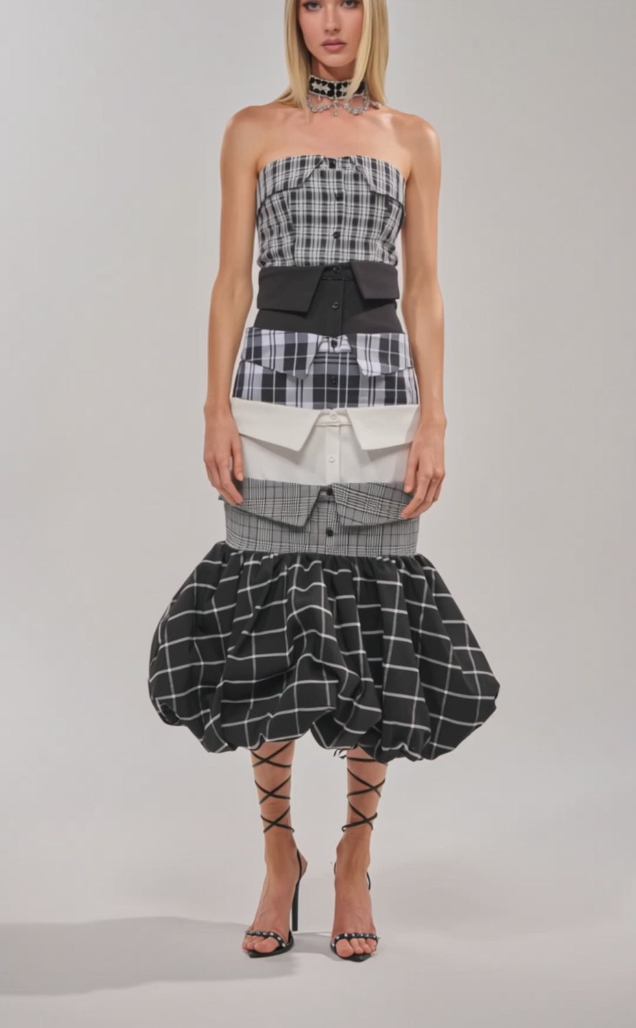 Video of woman modeling the CHANGING IT UP PLAID MIDI DRESS, a strapless midi with a fitted bodice, cinched waist, voluminous bubble hemline in mixed plaids, paired with strappy black high-heeled sandals.
