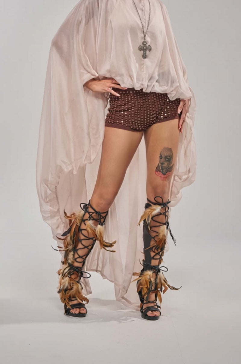 A video of a woman in the HEAD IN THE CLOUDS CHIFFON BLOUSE, patterned shorts, feathered black lace-up boots, and statement jewelry. 