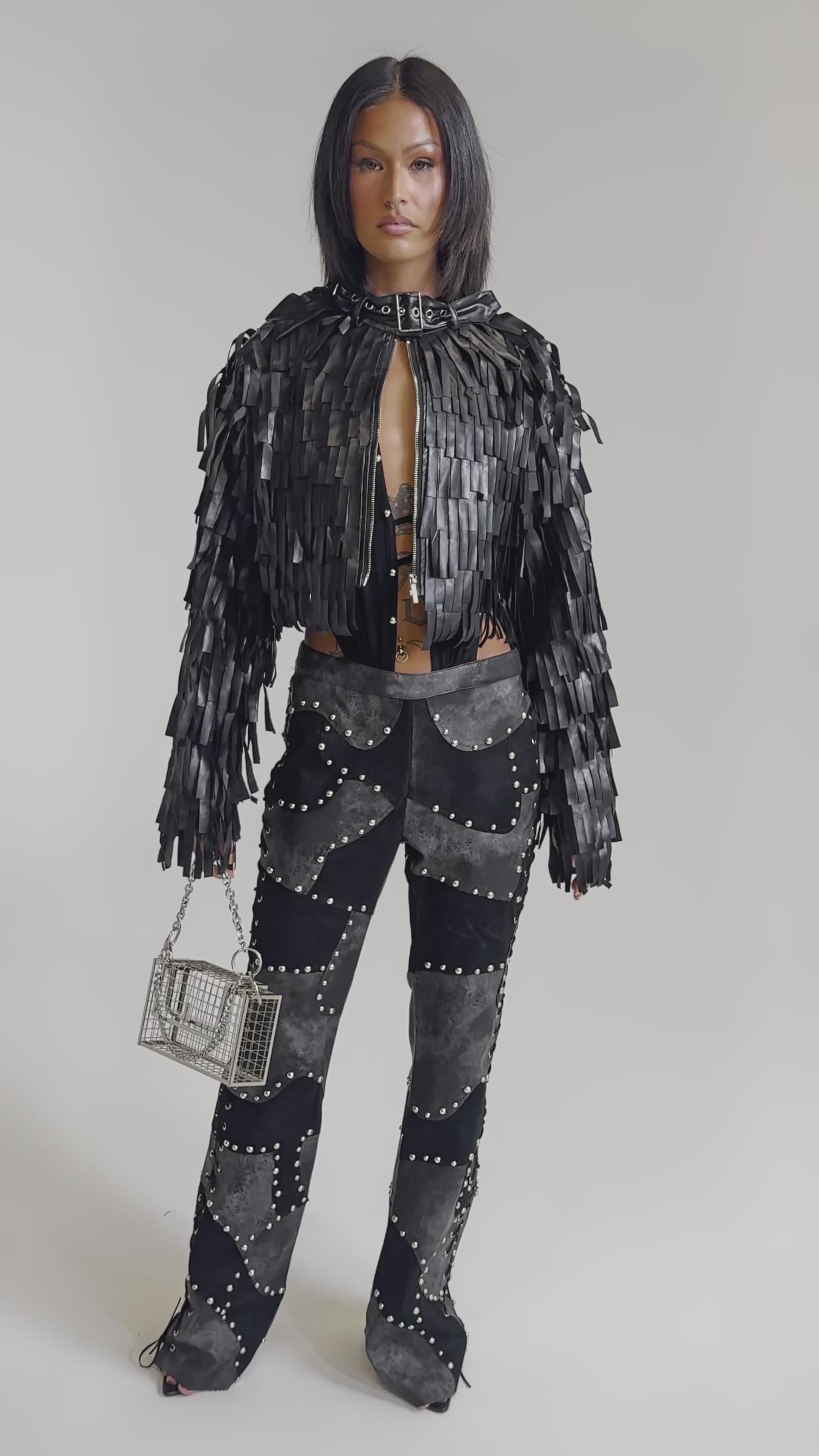A video of a woman in the RIDE EM FRINGE MOTO black jacket, studded black and gray pants, and black heels against a light background.