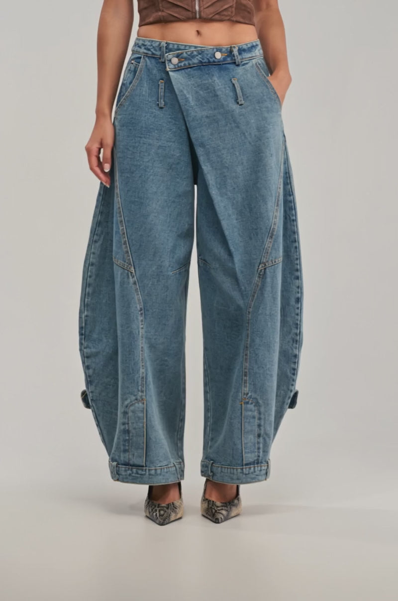 Video of a woman modeling the IZZY RELAXED DENIM IN LIGHT BLUE WASH, a person showcases wide-leg barrel jeans with a unique folded front design. 