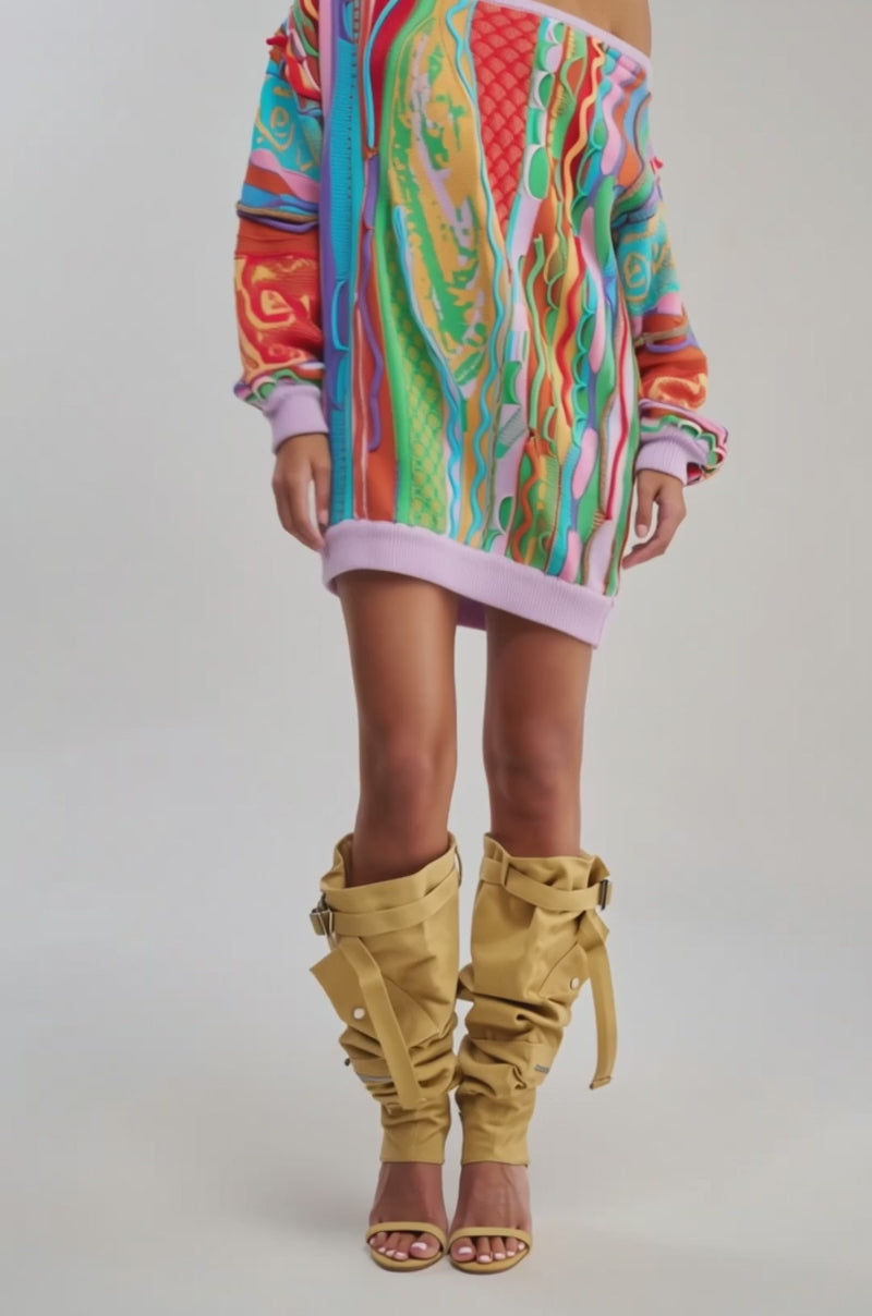 Video of woman modeling the CROWD FAVORITE SWEATER MINI DRESS—an oversized, off-the-shoulder piece with bold, textured red, orange, green, blue, and purple patterns—standing against a plain light background for vibrant winter style.