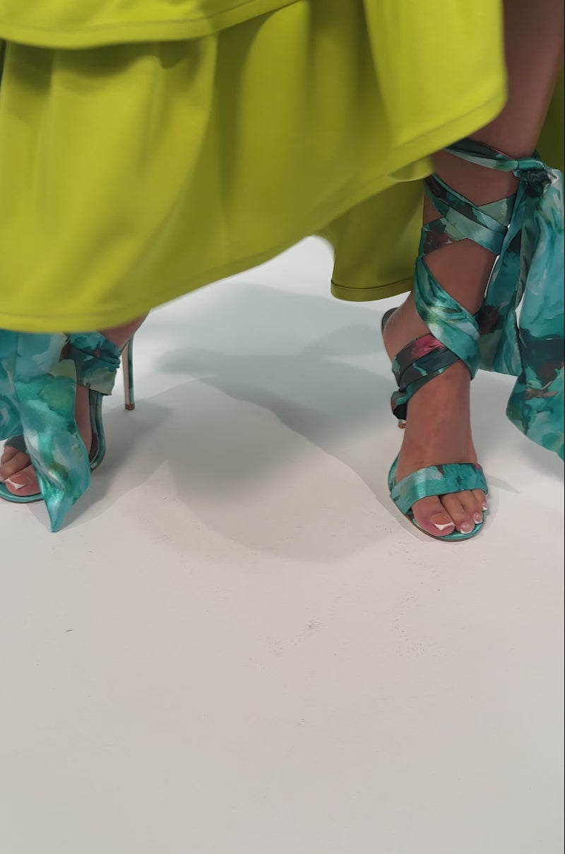 Video of woman modeling the AZALEA WANG ELZON GREEN SATIN STRAPPY SANDAL with teal floral details, wrap-around ankle straps, and a sleek stiletto heel.