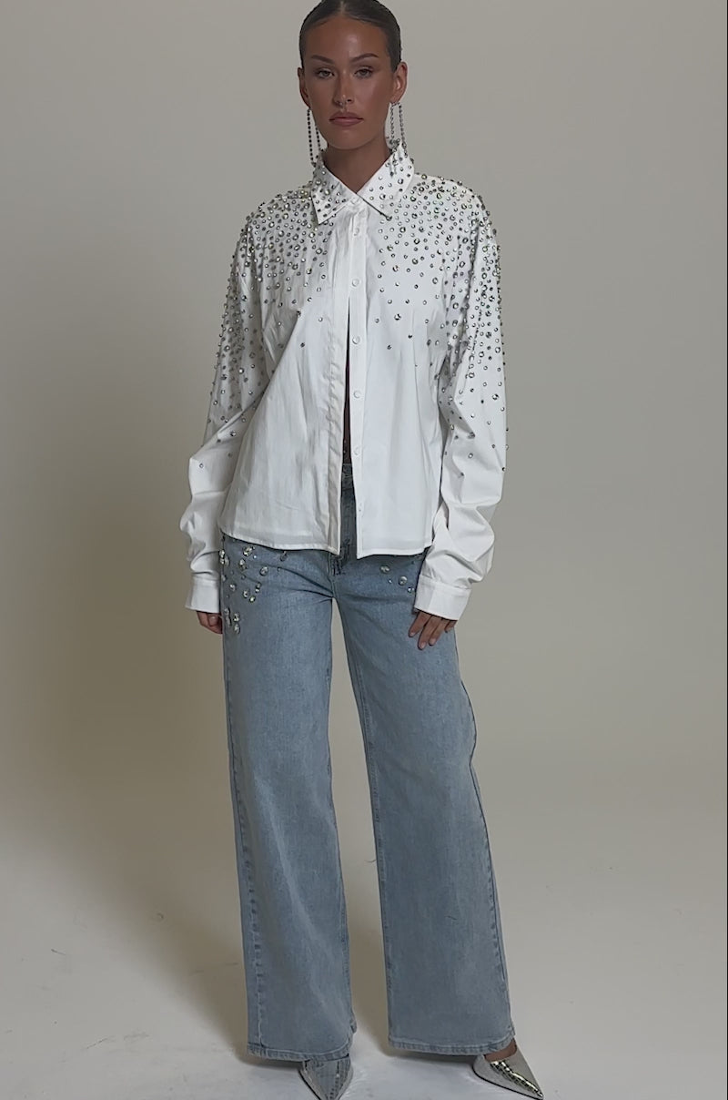 Video of woman modeling the ITS THAT TIME EMBELLISHED RELAXED DENIM—light blue wide-leg jeans with silver embellishments on the hips and thighs—styled with a white shirt and silver pointed-toe heels.