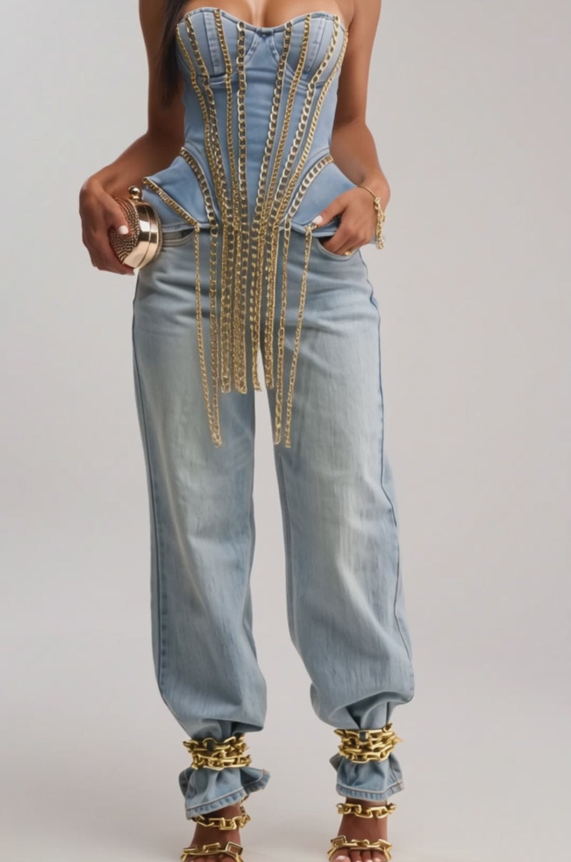 A video of a woman in the CHAINED DOWN CORSET, featuring gold chain link detailing, paired with matching denim pants and a small gold clutch against a plain light background.