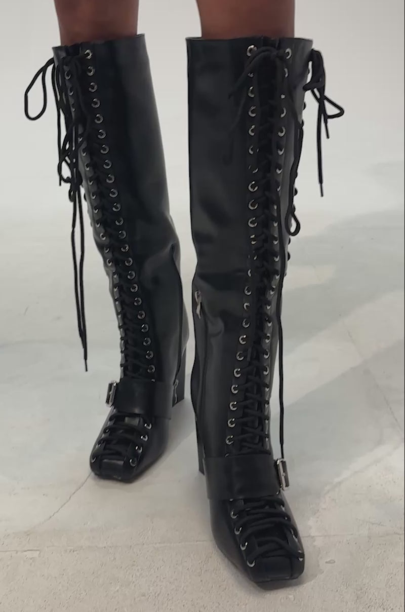 Video of woman modeling the AZALEA WANG FLICKER BLACK BLOCK LACE UP BOOT—knee-high, crafted from sleek black faux leather, featuring chunky block heels, lace-up fronts, and side zippers