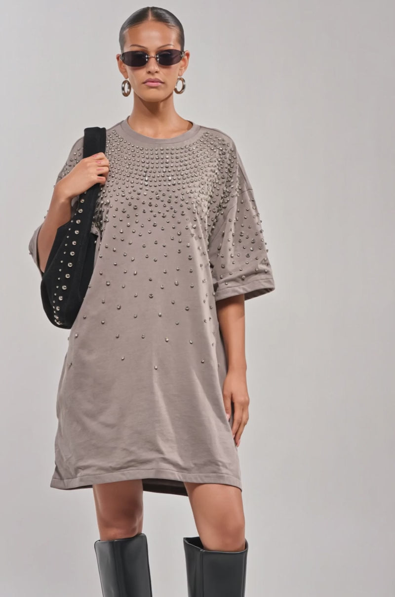 Video of woman modeling the IN MY ELEMENT RHINESTONE TEE SHIRT MINI DRESS, sunglasses, black slouchy knee-high boots, and holding a black bag posing confidently against a plain background.