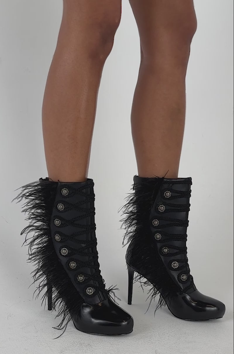 Video of a woman modeling the AZALEA WANG BANSHEE BLACK MILITARY AND FEATHER STILETTO BOOTIE, which features a lace-up front, feather detailing along the sides, and decorative buttons.