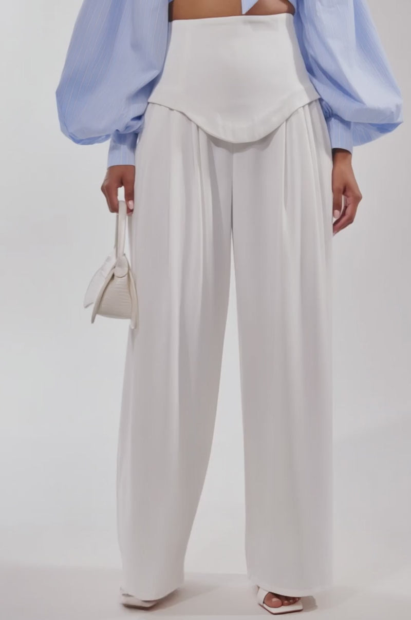 A video of a person wearing GALAXY TROUSER high-rise white wide-leg trousers, a light blue puff-sleeve top, white heeled sandals, and holding a small white handbag.
