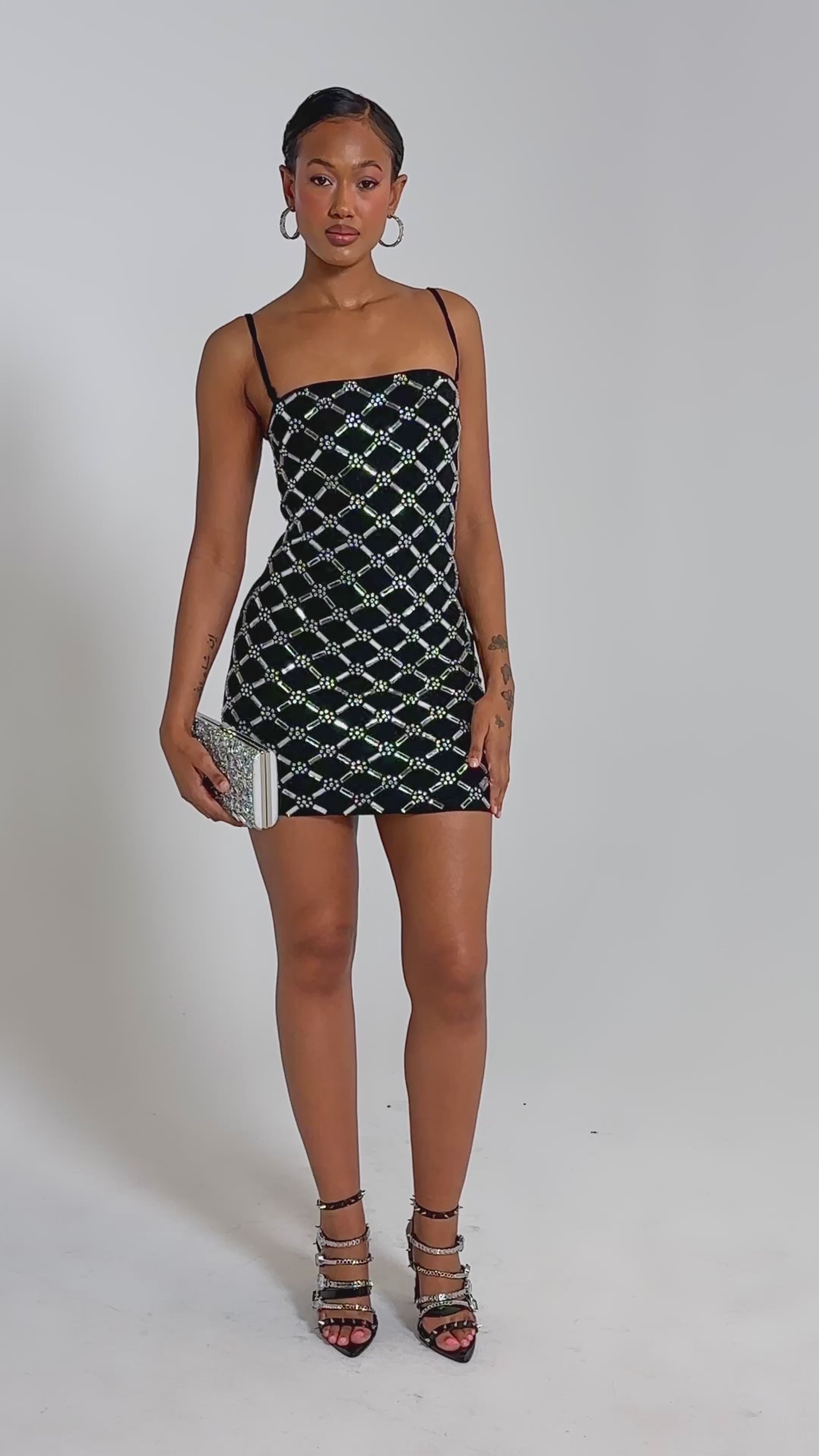 A video of a woman in the SPARKLE CITY RHINESTONE MINI DRESS with a silver diamond pattern, holding a silver clutch and wearing strappy heels, against a plain light background.