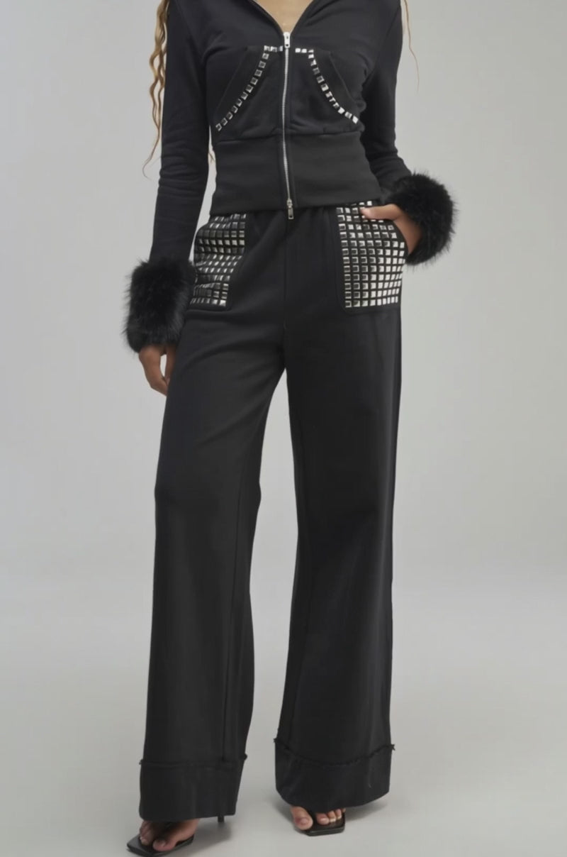 Video of a woman modeling the BLESSED ZIP UP SWEATSHIRT—a black hoodie featuring faux fur trim and silver stud details.