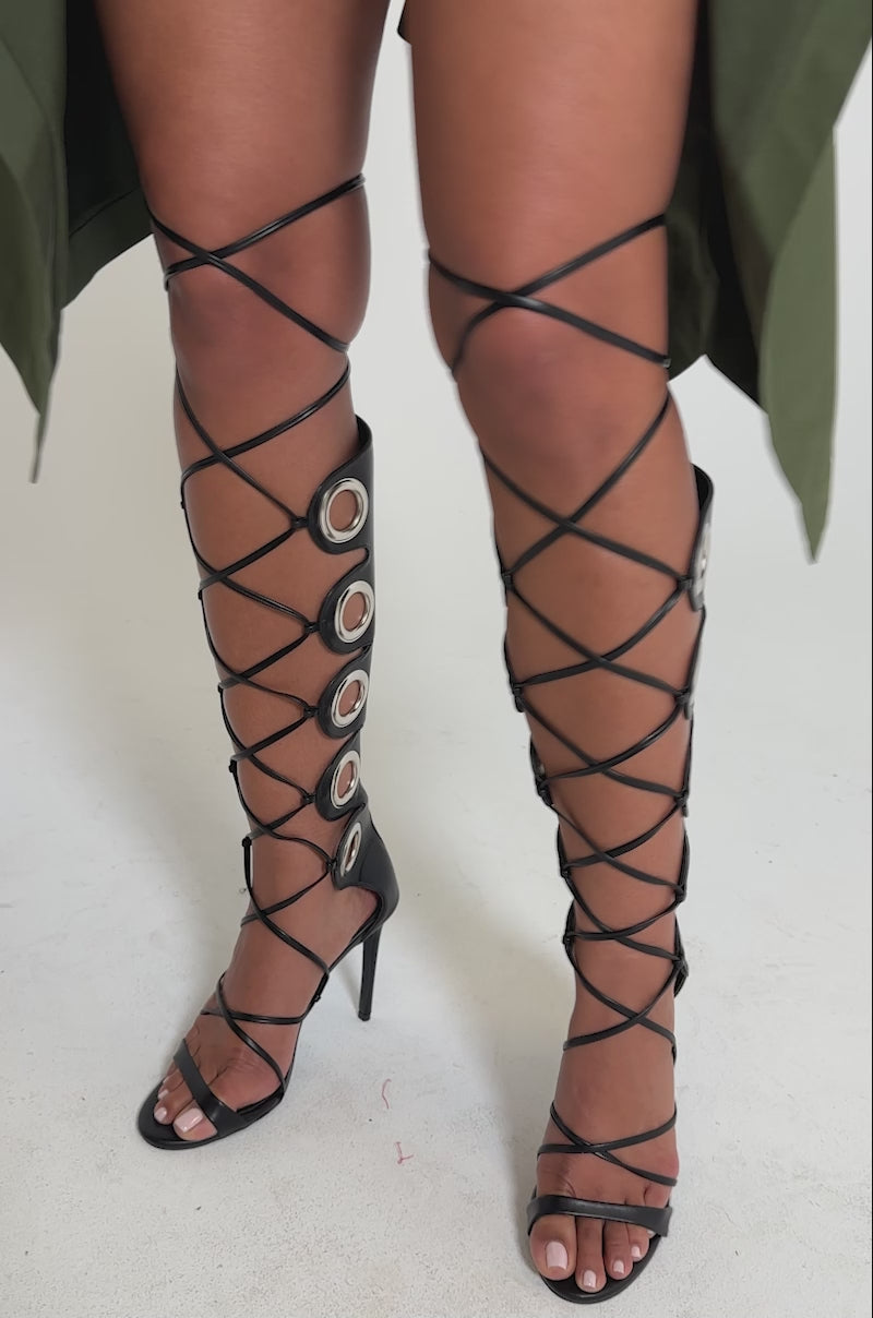 A video of a model wearing the AZALEA WANG AGATHON Black Gladiator Stiletto Sandal with silver eyelets and open toes.