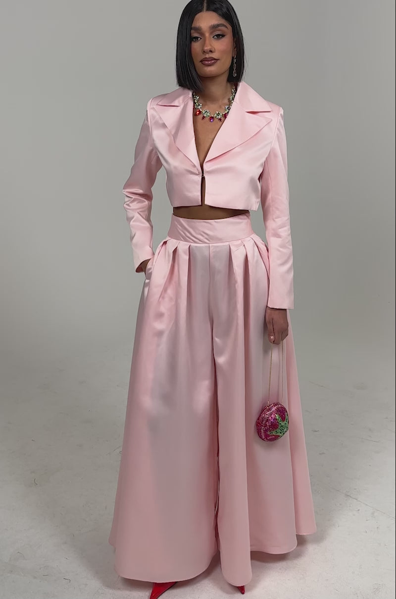 Video of woman modeling the LILA SATIN BLAZER in blush pink, cropped and tailored, paired with matching high-waisted pleated pants, colorful necklace, and pink earrings against a simple light background.