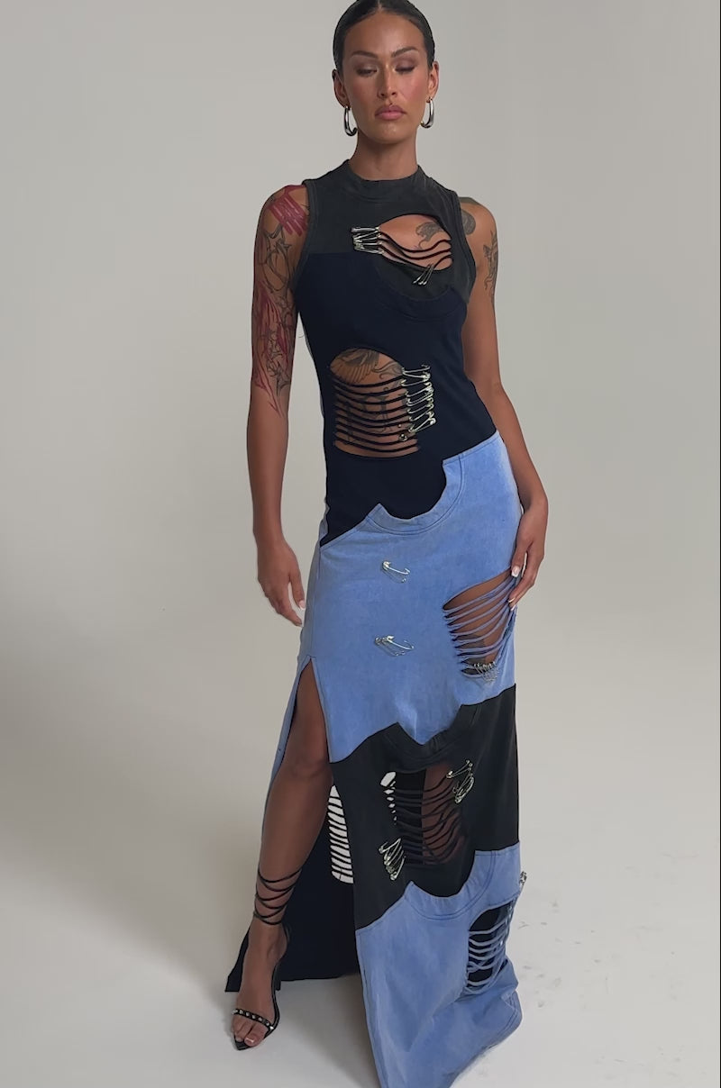 Video of woman modeling the LAST MINUTE MASTERPIECE DISTRESSED MAXI DRESS, featuring bold cutouts, safety pins, and shredded details. She pairs it with strappy heels and shows off her tattoos against a plain light background.