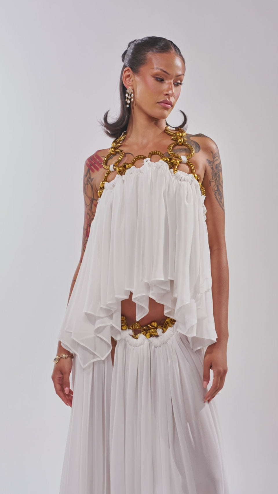 Video of woman modeling the DESERT VIBES BRALETTE, a white organza halter top with gold hardware, paired with gold statement earrings. 