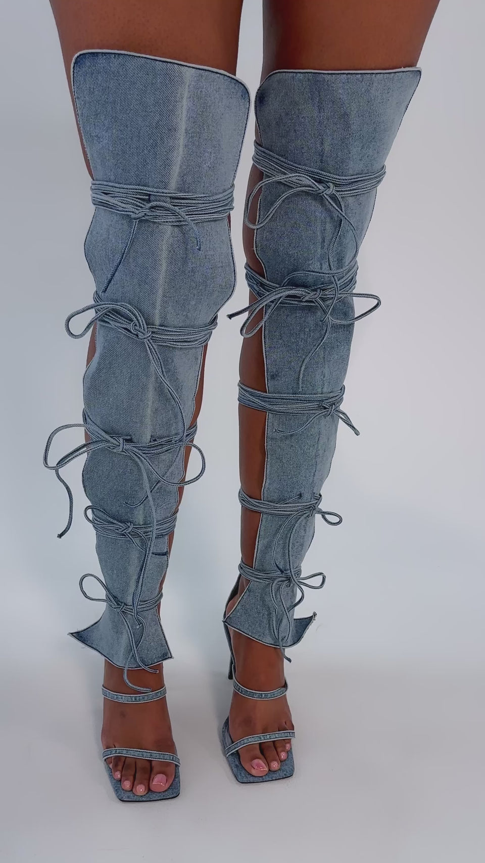 A video of a person wearing the AZALEA WANG KRISTINE DENIM STILETTO GLADIATOR SANDAL—light blue, thigh-high, open-sided denim boots with denim laces and a matching open square toe high heel.