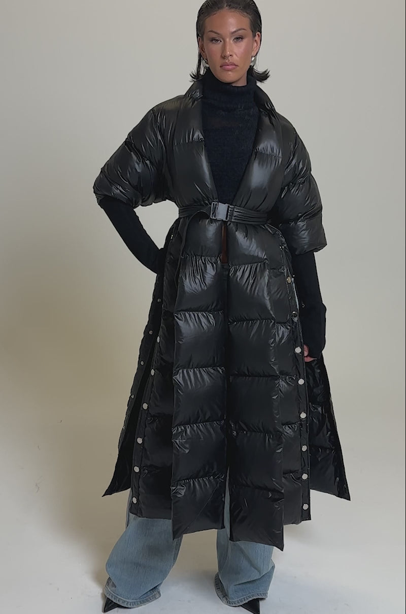 A video of a woman in the POPPIN OFF TEARAWAY PUFFER, styled with a black turtleneck sweater and wide-leg blue jeans against a plain light gray background.