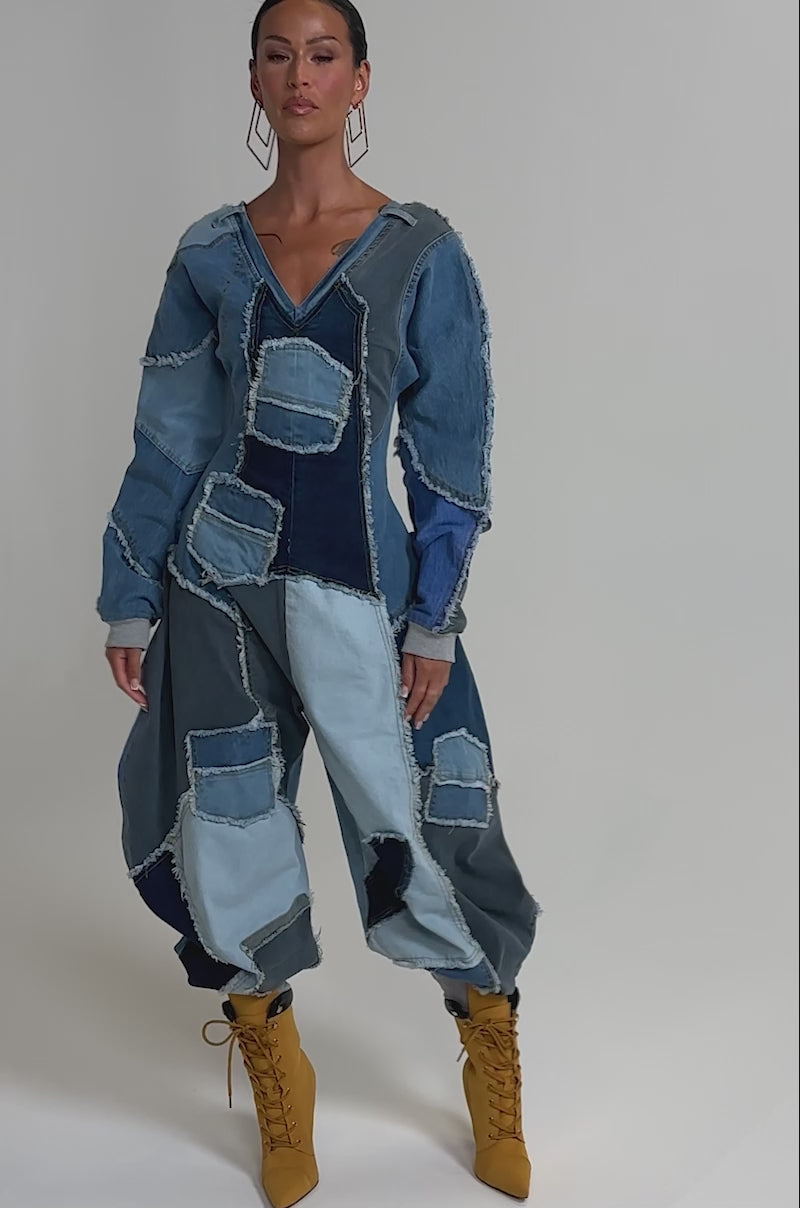 Video of woman modeling the COMFY COZY JUMPSUIT IN DENIM PATCHWORK, featuring various blue hues and raw edges, paired with large hoop earrings and mustard yellow lace-up boots against a plain light background.